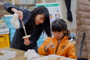 大学生に教わりながら糸をつむぐ女の子