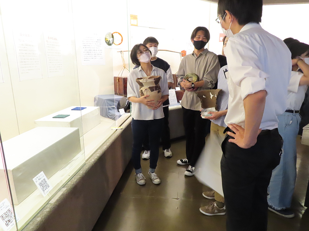 展示ケースの前で展示に使用した土器を持ち学芸員と相談する実習生