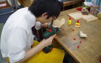 新宮学芸員がドリルで縄文土器(会員が製作したもの)に穴を開けている様子