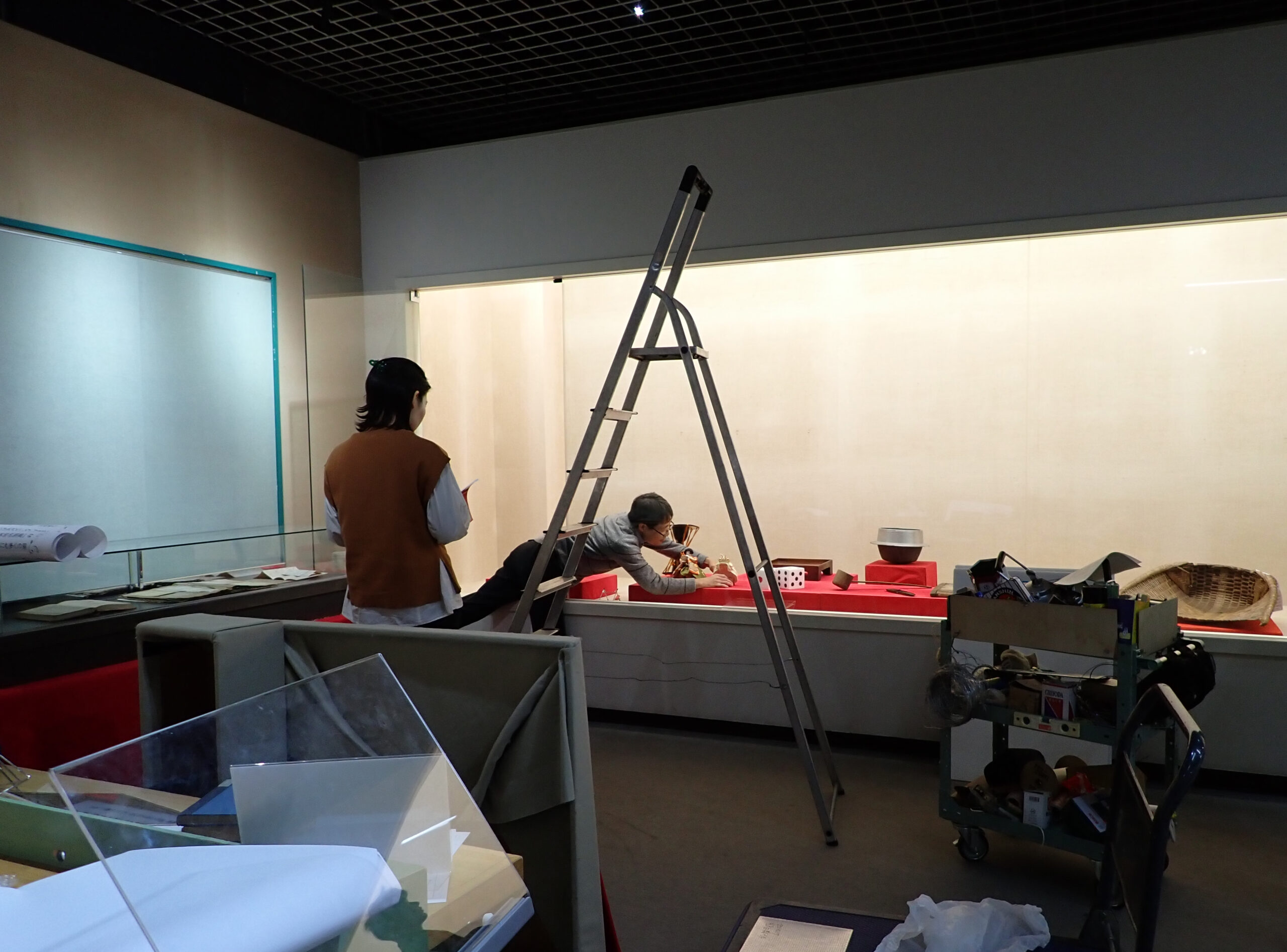 展示ケース内の資料を調整するようす。展示ケースの外には工具箱や脚立があり、正に作業中といった様子。