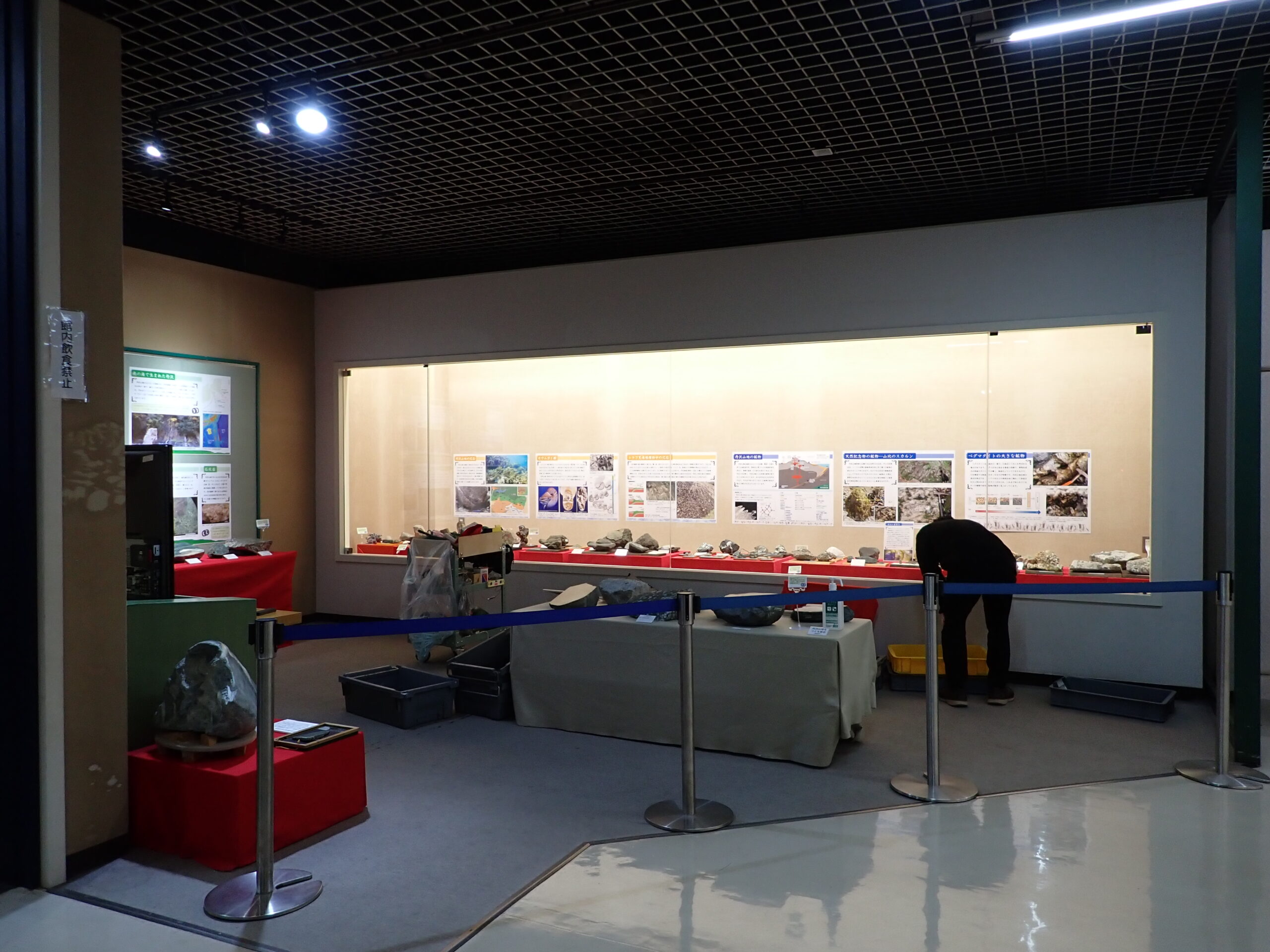 展示作業をしている様子。手前にパーテーションがあり、奥が展示ケース。展示ケース前のスペースには磨かれた石材が並ぶ。
